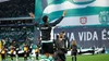 Ein Spieler im Sporting-Trainingsanzug läuft mit erhobenen Armen im vollen Stadion auf den Rasen ein, begleitet von Einlaufkindern vor einem riesigen Fanbanner.